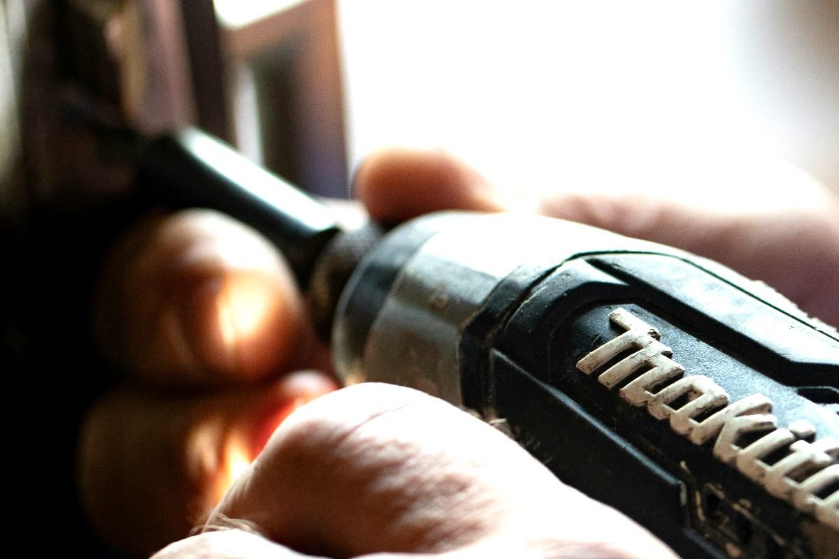 A hand holding a cordless drill at the edge of a door during a call-out